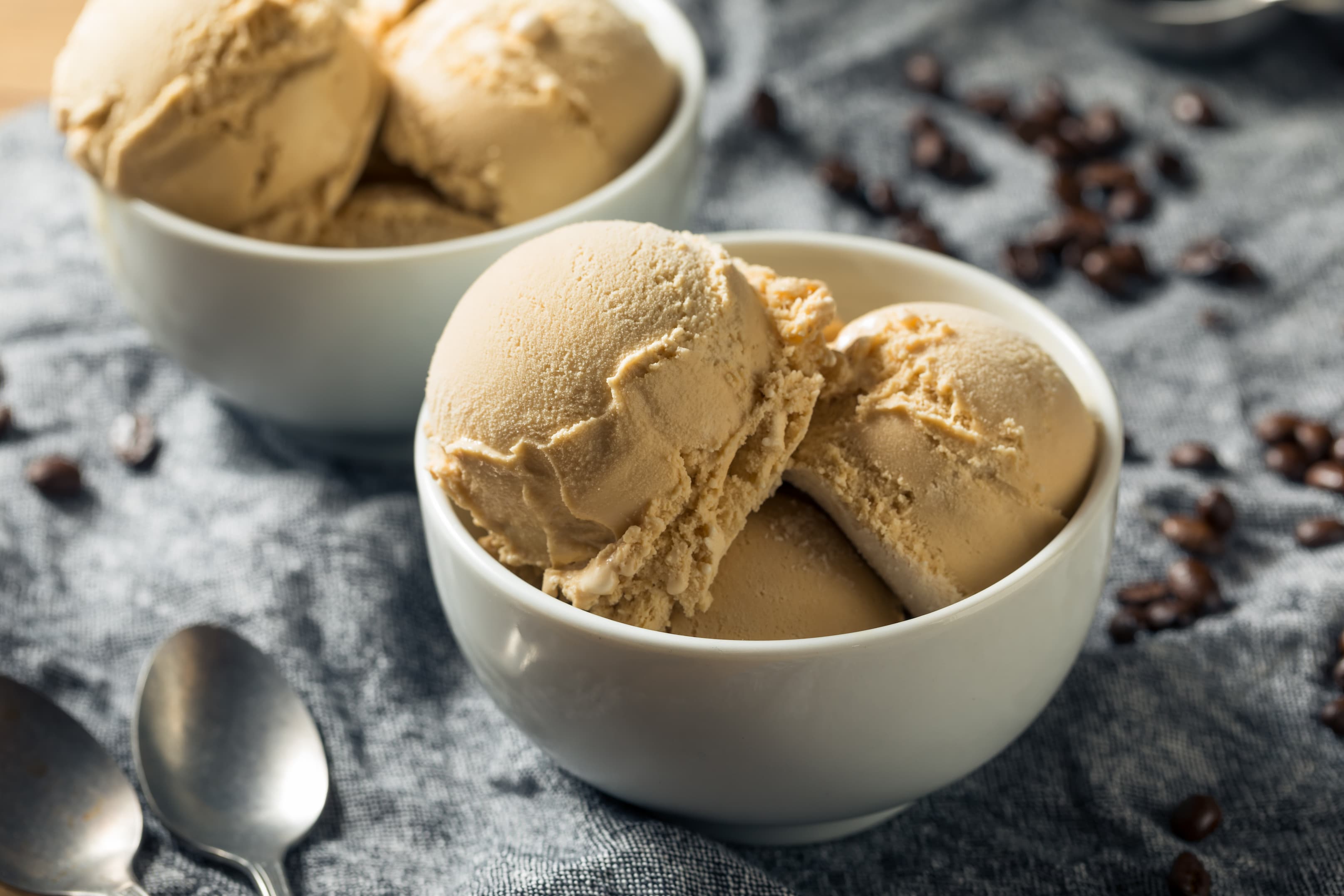Schale mit Kugeln aus cremigem Kaffee-Eis, serviert auf grauem Stoff mit Kaffeebohnen.