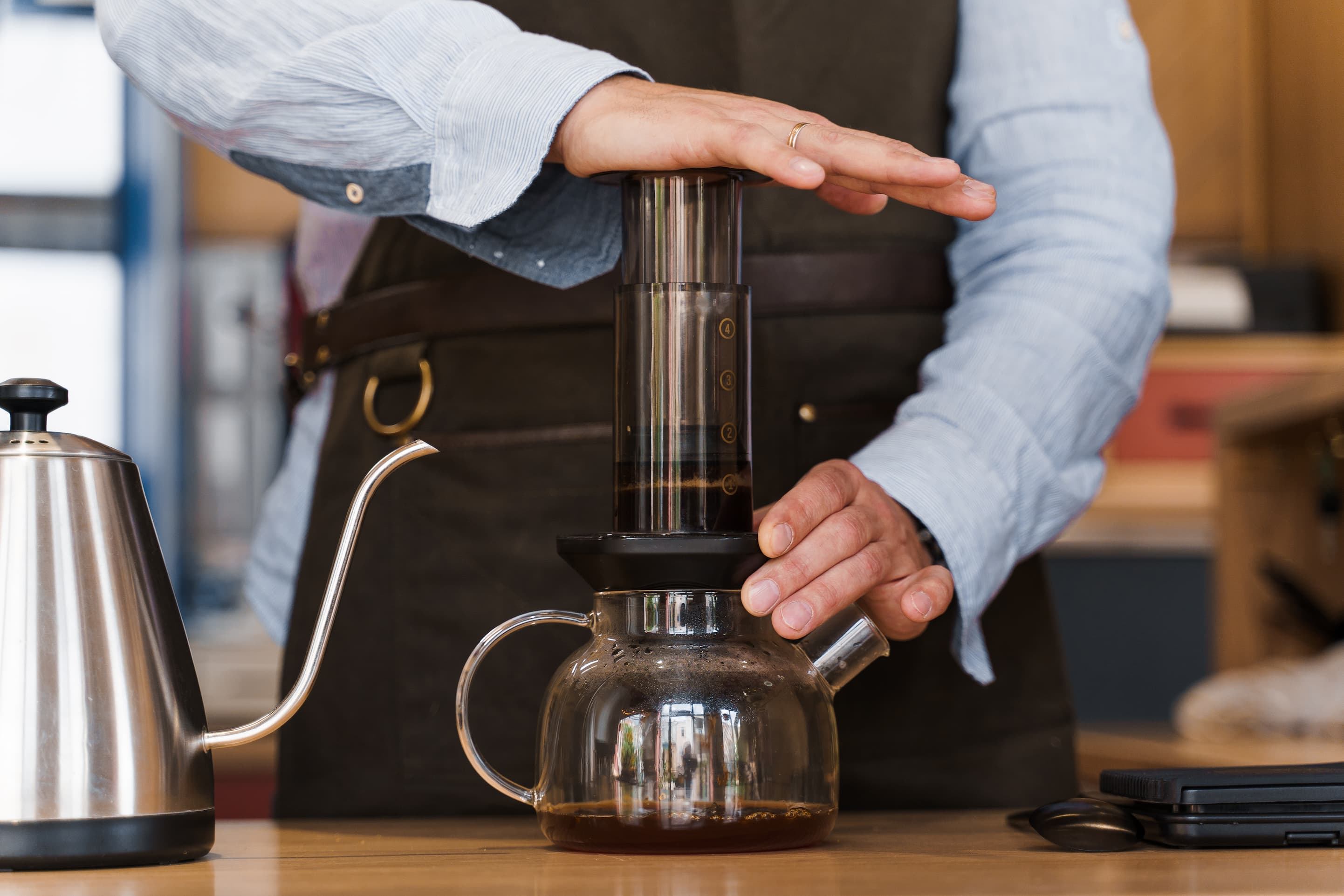 Barista bereitet Kaffee auf traditioneller Art in Glas-Kanne auf Holztisch zu.