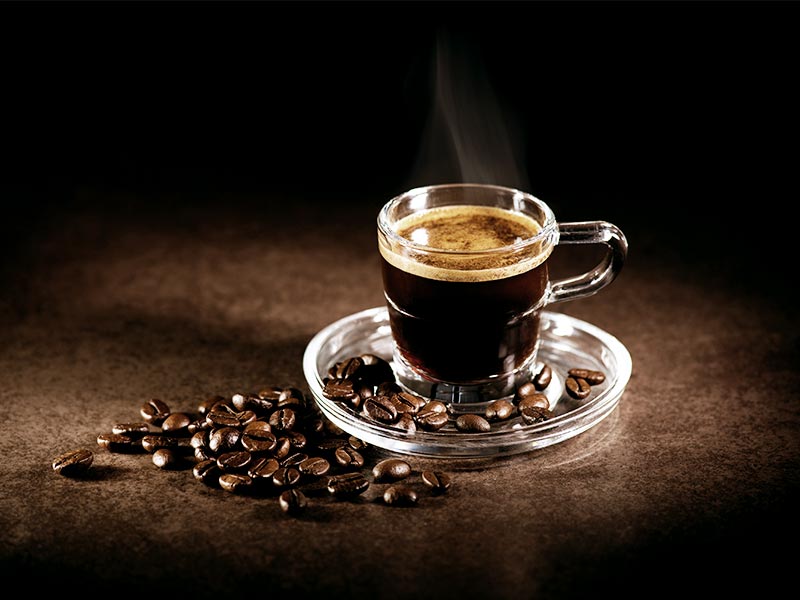 Eine Tasse frisch gebruehter Kaffee mit Kaffeebohnen auf einem dunklen Untergrund.