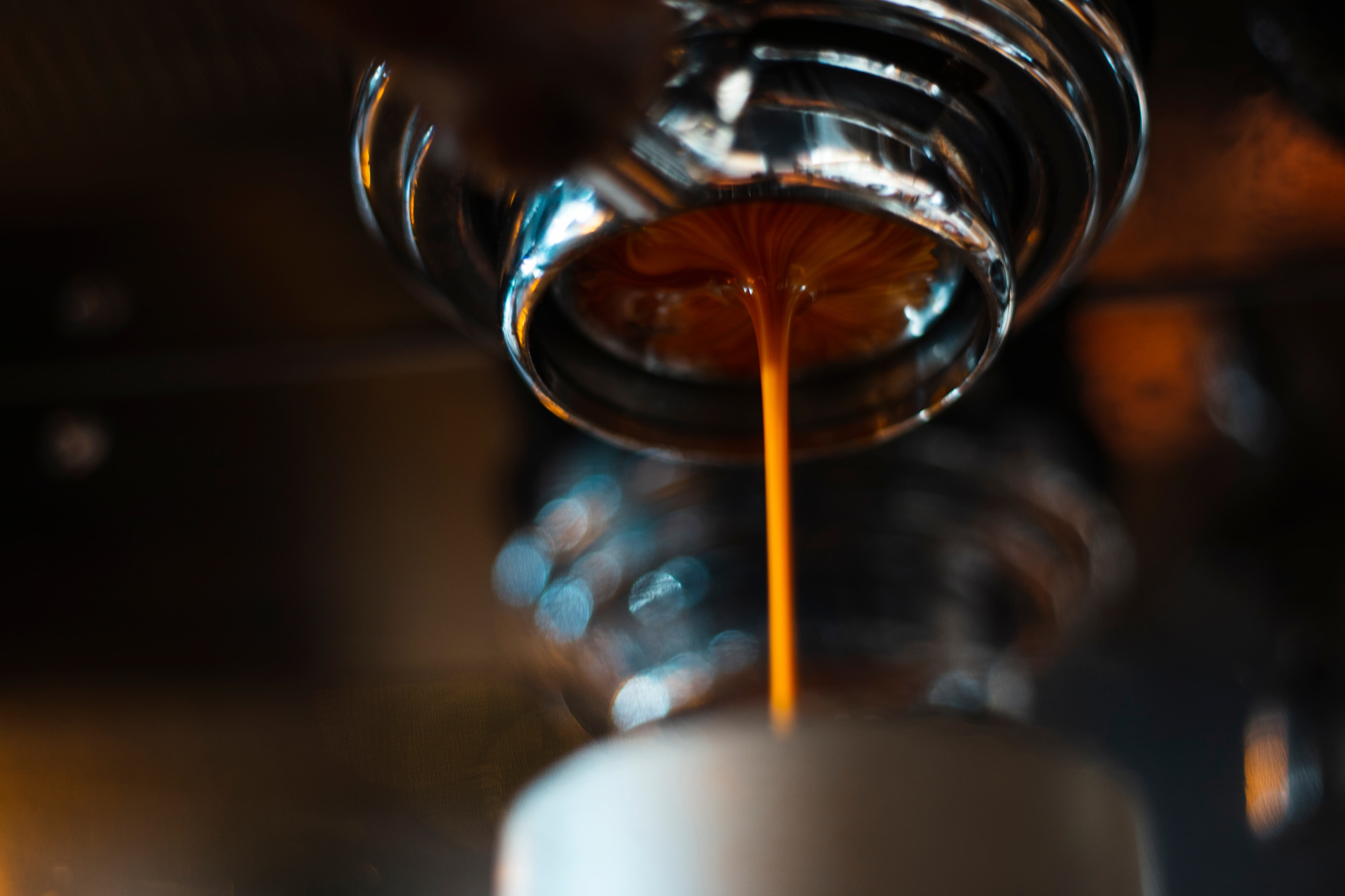 Frisch gebruehter Espresso laeuft aus einer Siebtraegermaschine in eine Tasse, Nahaufnahme.