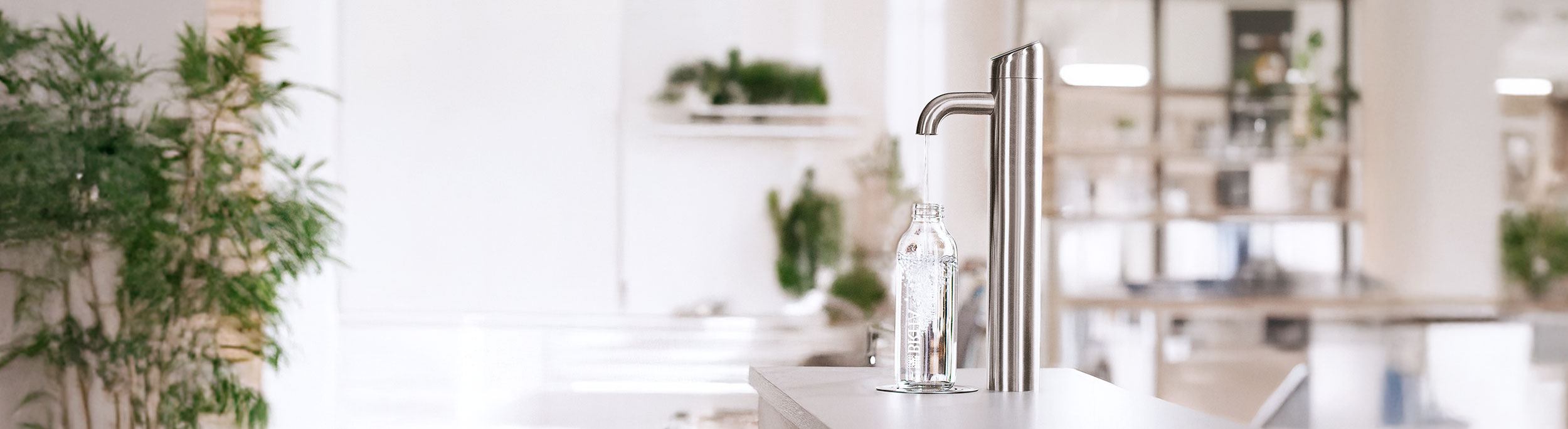 Edelstahl-Wasserhahn fuellt Glasflasche in heller, moderner Bueroumgebung.