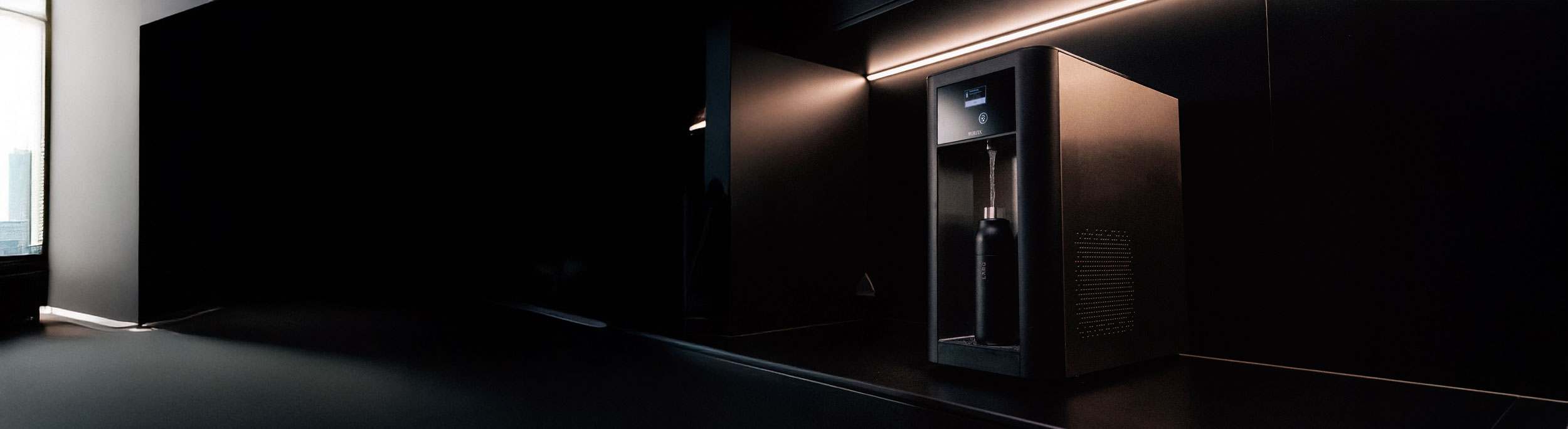Schwarzer BR50 Wasserspender in modernem Raum mit dunkler Wand und minimalistischer Beleuchtung, fuellt schwarze Flasche mit Wasser.