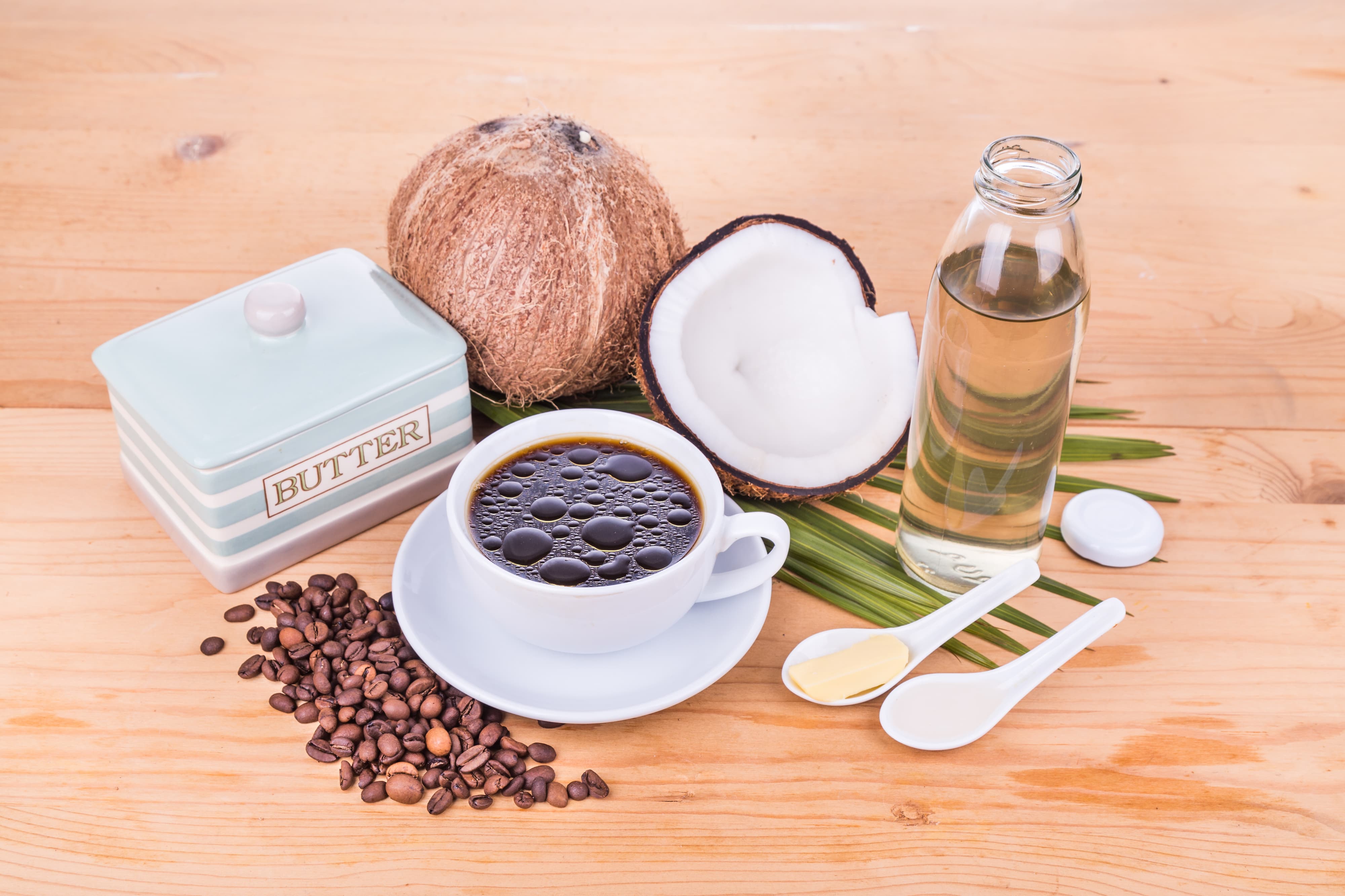 Tasse Kaffee mit Kokosnuss, Ölflasche, Butter und Kaffeebohnen – Bulletproof Coffee.