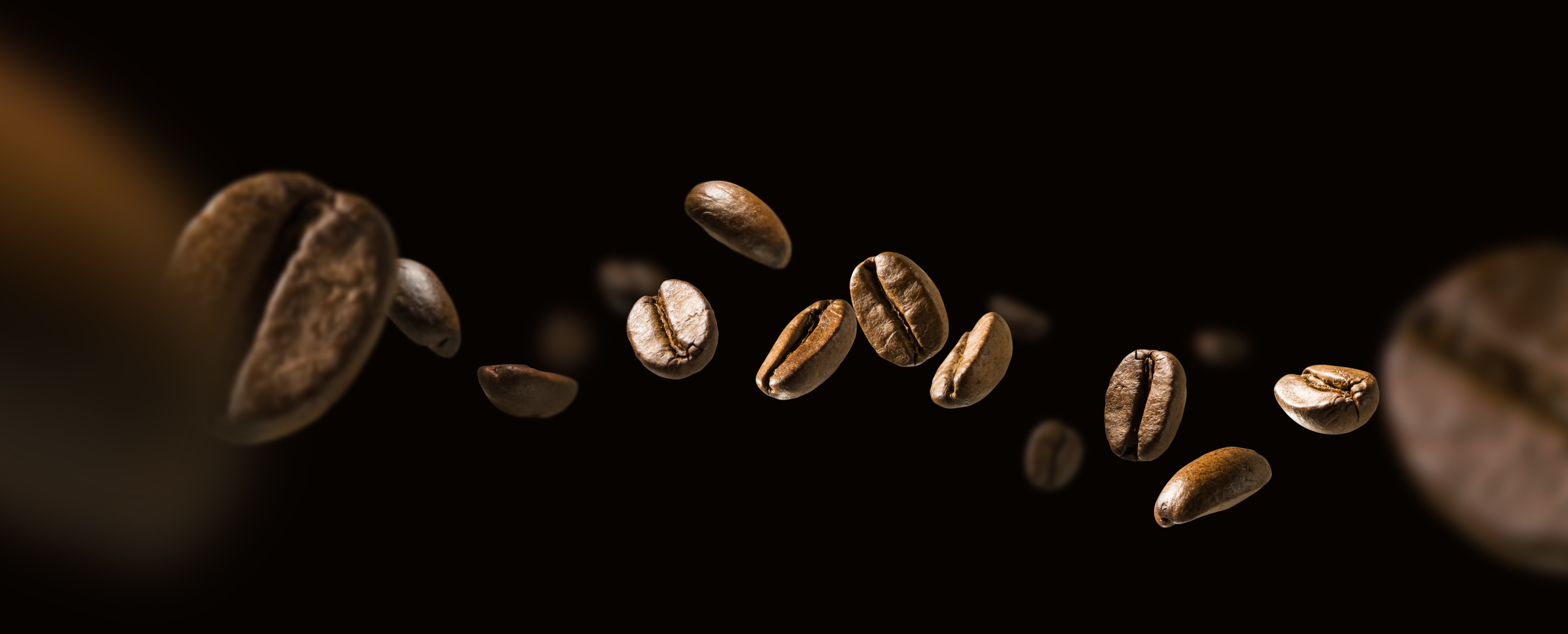 Nahaufnahme von fliegenden Kaffeebohnen auf schwarzem Hintergrund.