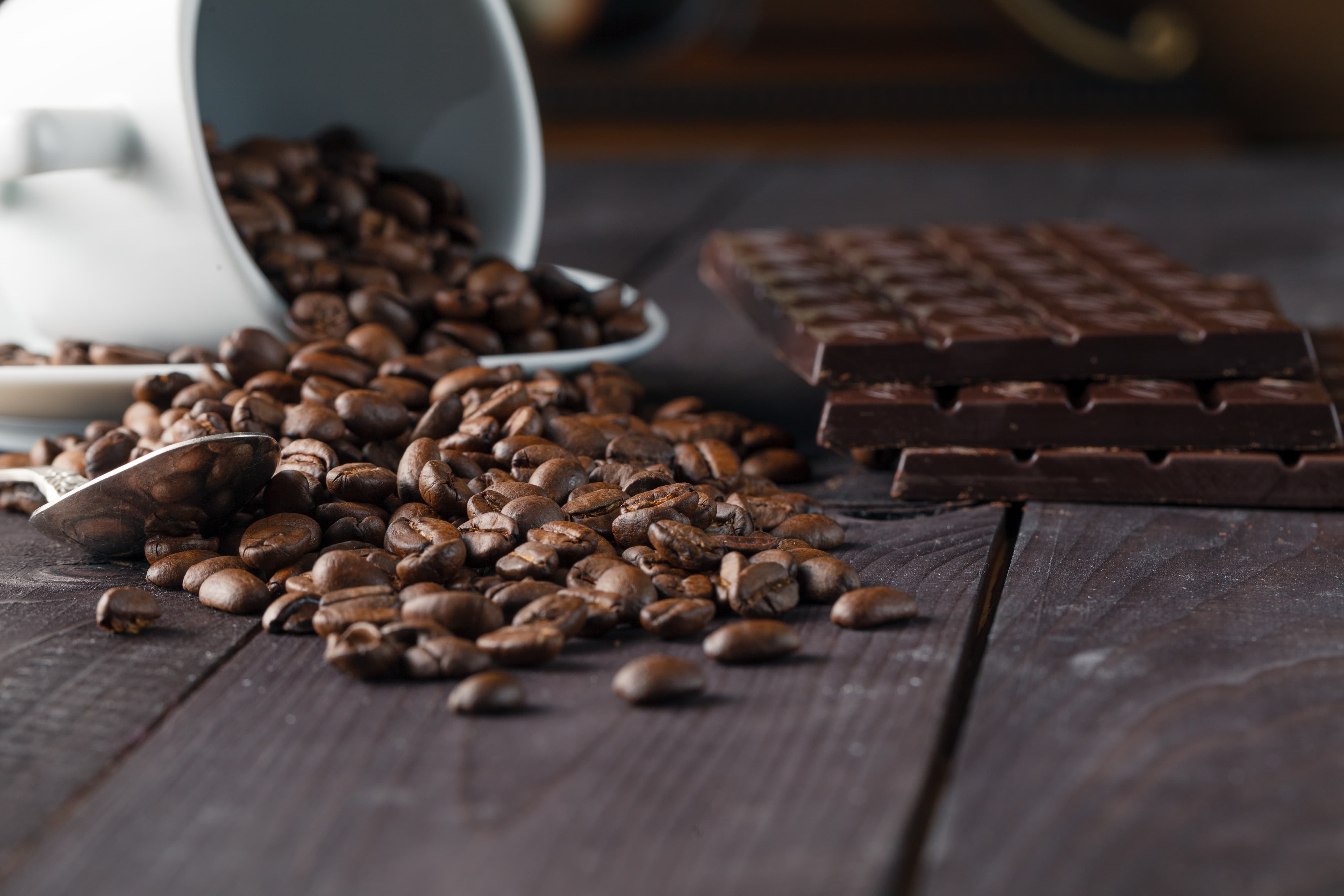 Frisch geröstete Kaffeebohnen vor gestapelten Tafeln dunkler Schokolade.