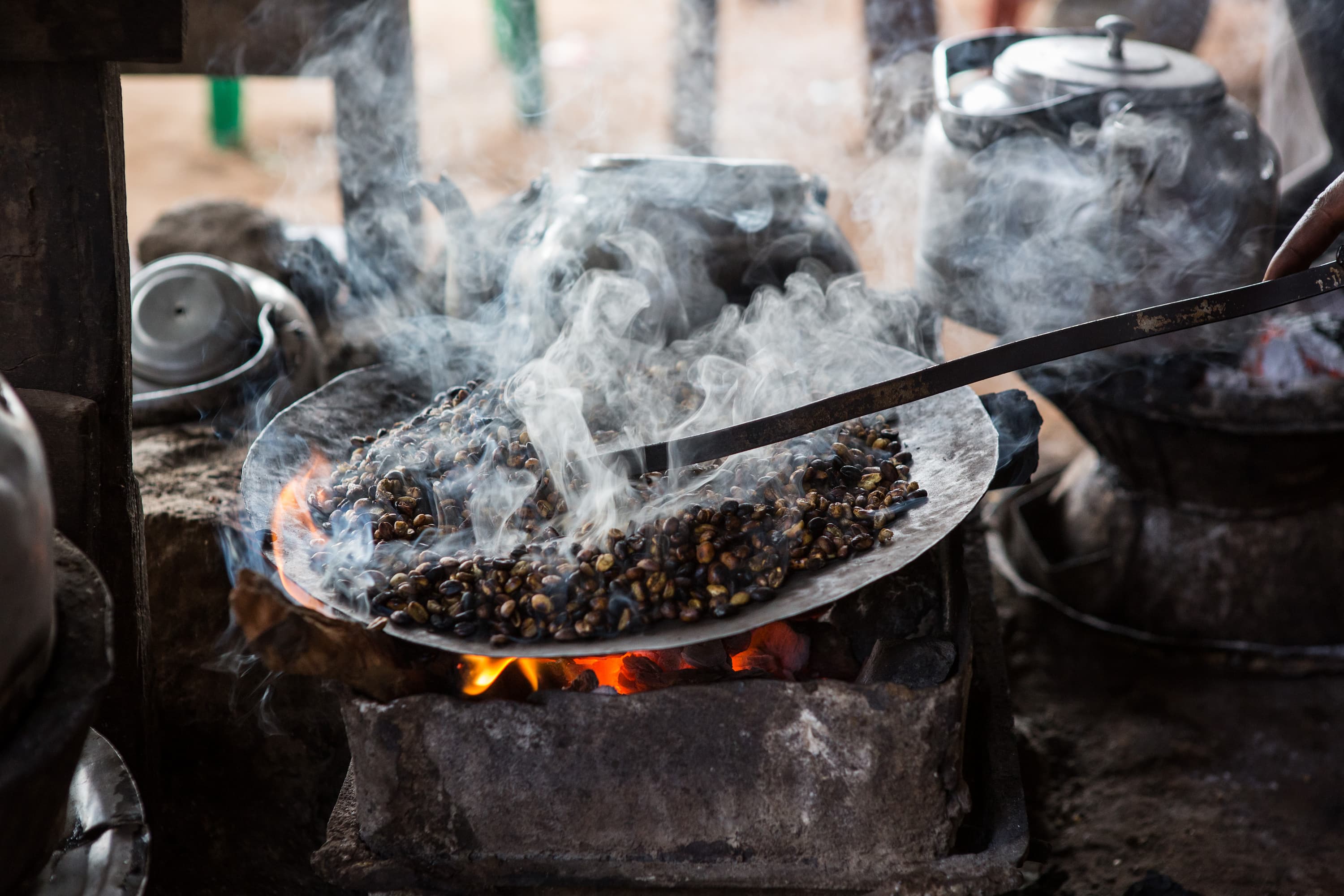 Frische Kaffeebohnen werden traditionell über Feuer geröstet, Rauch steigt auf.