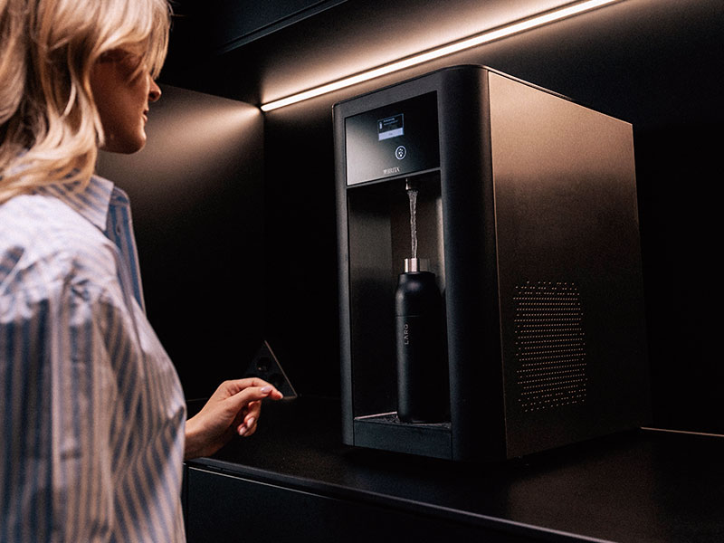 Frau befüllt ihre Trinkflasche an einem modernen BRITA BR50 Wasserspender in dunkler Umgebung.