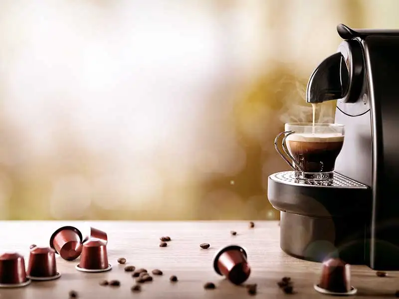 Kapselmaschine bereitet einen Espresso zu, Kaffeekapseln liegen daneben.